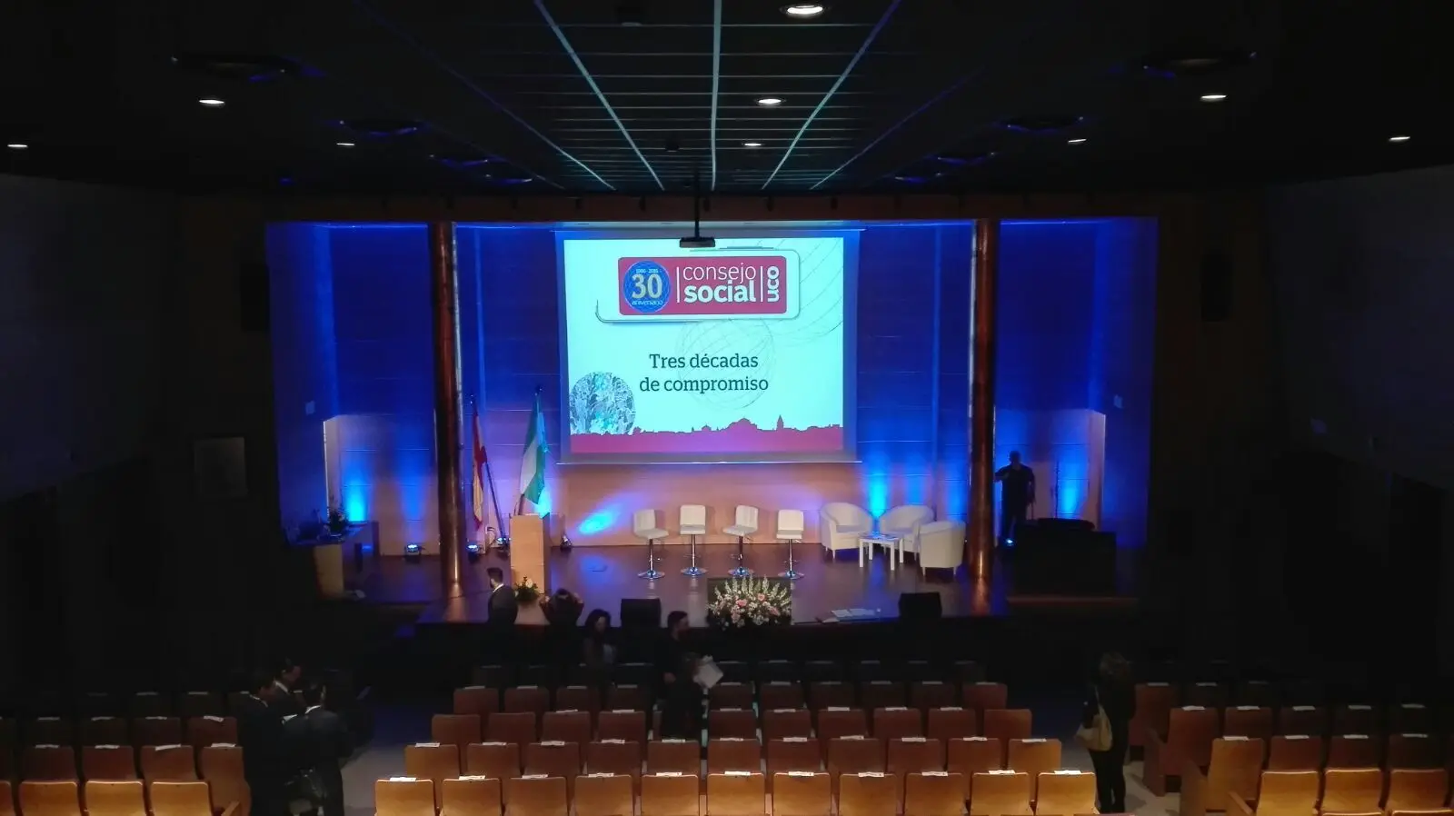 Escenario de una sesión plenaria iluminado en azul, con la mesa de ponentes y la pantalla