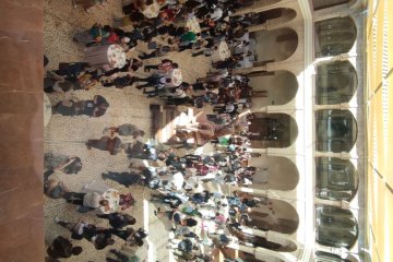 Vista desde arriba de asistentes de pie en una galería con arcos, durante un descanso del congreso.