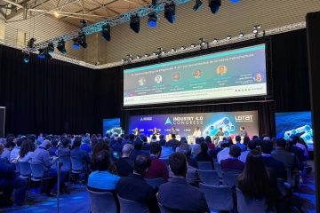 Sala llena en una sesión de congreso industrial: el público sentado mira a un panel de ponentes bajo los focos y una gran pantalla.