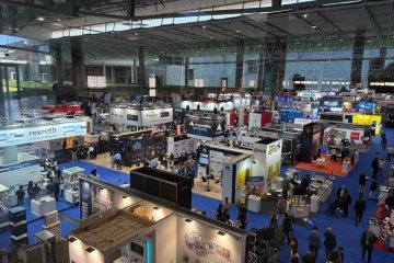 Vista desde lo alto del recinto de una feria industrial, con decenas de stands y visitantes recorriendo los pasillos.