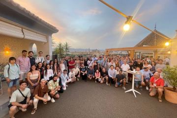 Foto de grupo de más de un centenar de asistentes a una reunión científica, en una terraza al atardecer con la ciudad al fondo.