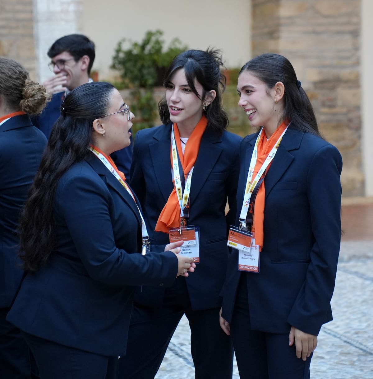 Personal de sala de Esmeeting, con traje azul y pañuelo naranja: tres de ellas conversan en un patio.