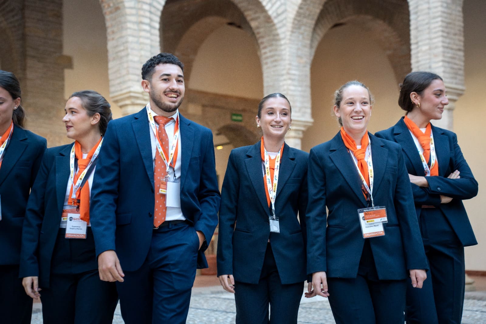 Integrantes del personal de sala de Esmeeting, con traje azul y pañuelo naranja, caminan por el patio de una sede.