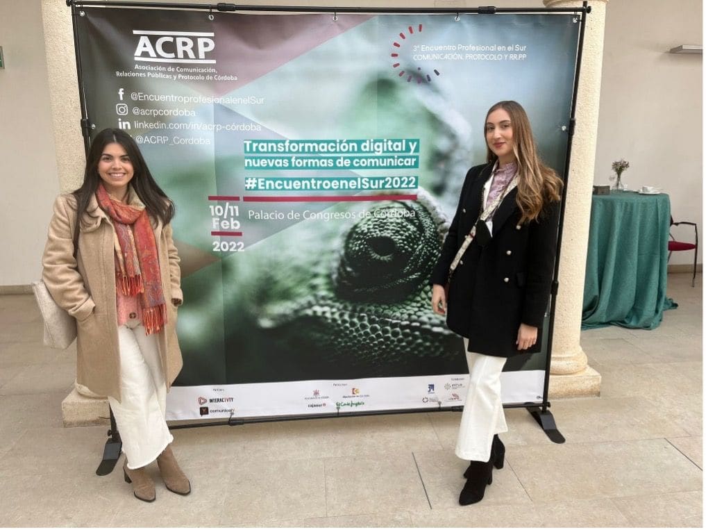 Dos asistentes junto al panel de un encuentro científico, con la imagen del congreso.