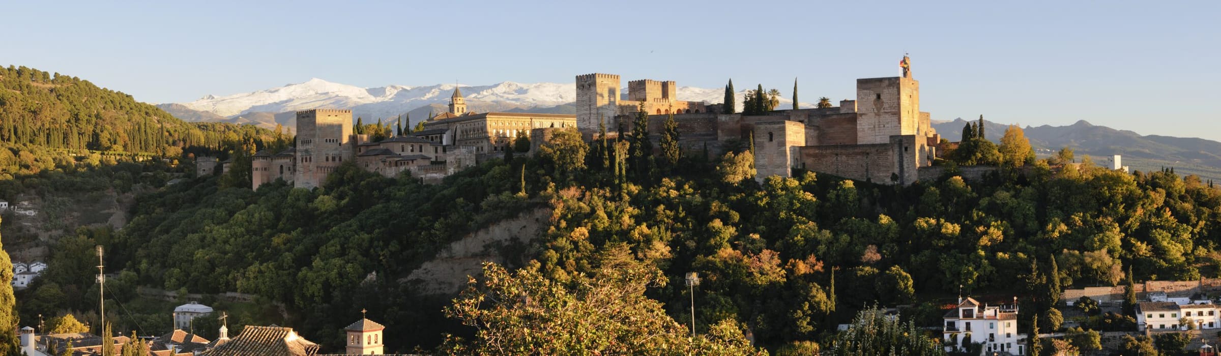 La Alhambra de Granada entre arboleda, con Sierra Nevada al fondo.