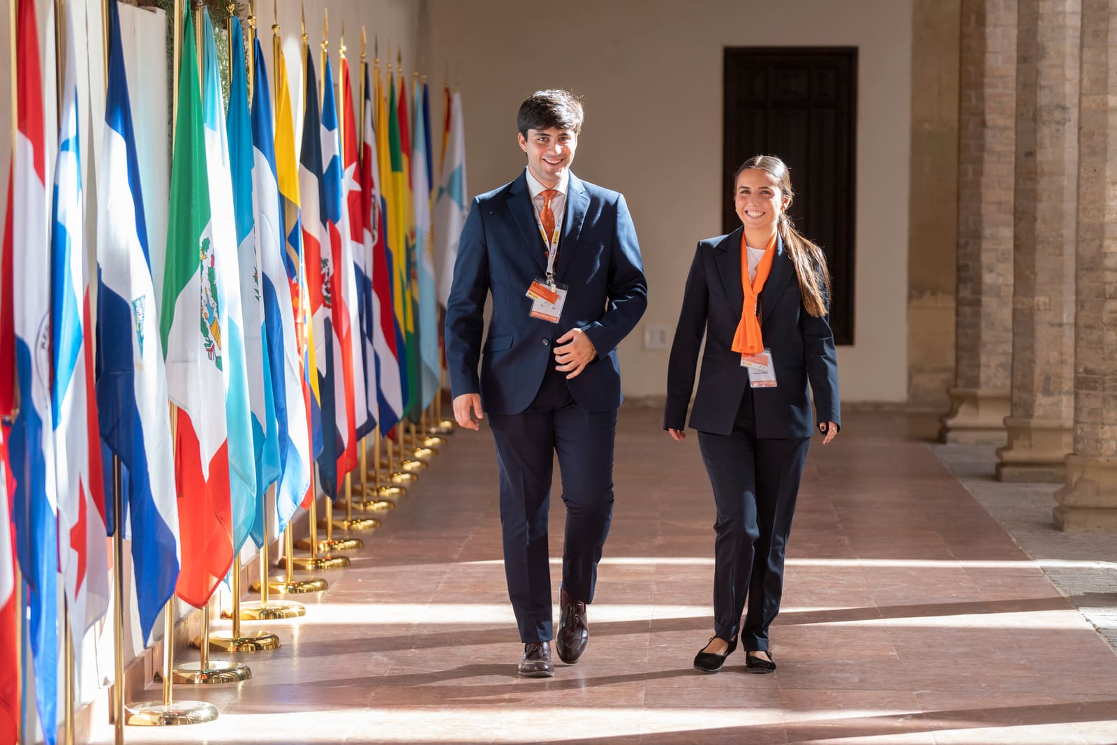 Dos personas de la organización caminan por el pasillo de banderas de la Cumbre Internacional.