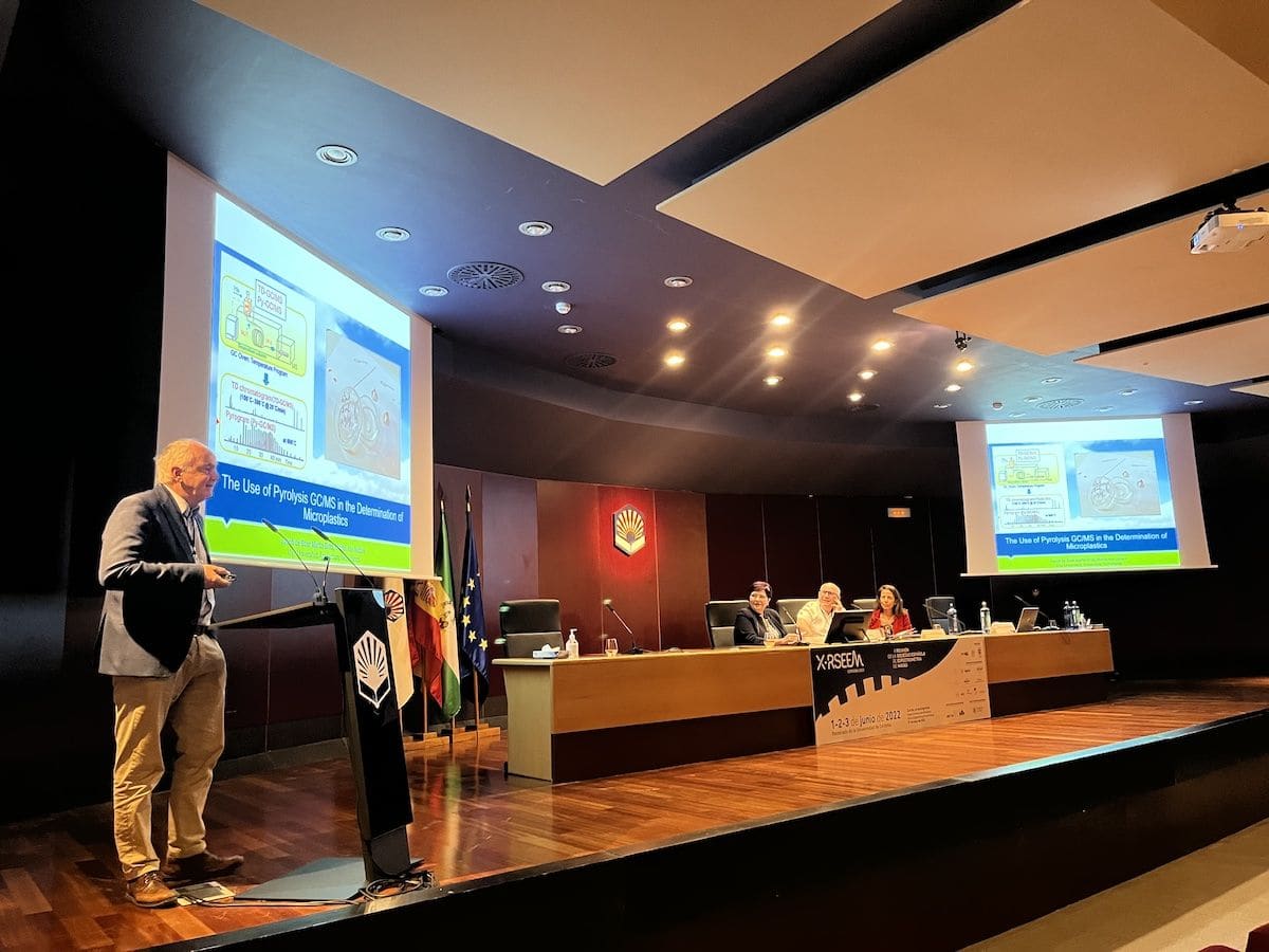 Un ponente presenta ante la mesa y la sala en un congreso científico.