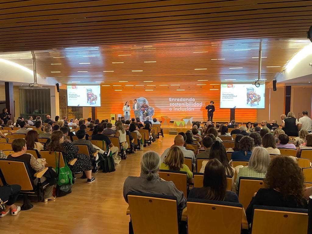Sala llena en una jornada sobre sostenibilidad e inclusión, con el escenario en tonos naranjas.