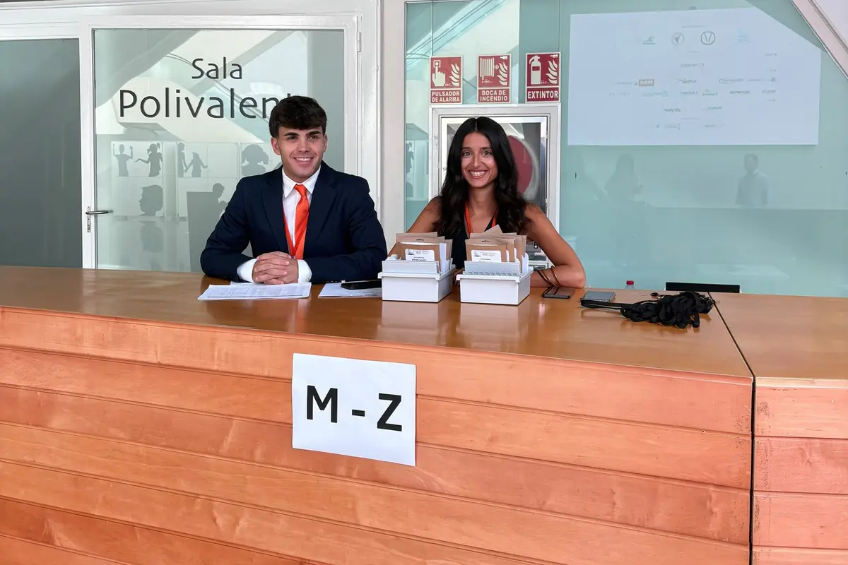 Dos personas atienden un mostrador de recepción de un congreso